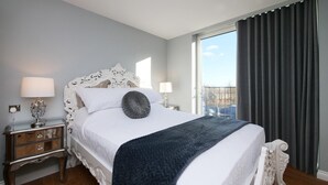 Ein Hotelzimmer mit einem großen Bett, zwei Nachttischen, einem Schminktisch und einem Balkon mit Vorhängen.