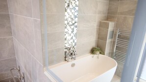 Ein modernes Badezimmer mit einer freistehenden Badewanne, einer Duschkabine aus Glas und einer mit Fliesen verkleideten Duschwand.