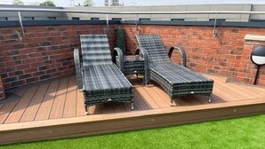 A rooftop deck with two lounge chairs and a small table, surrounded by a brick wall and a wooden deck.