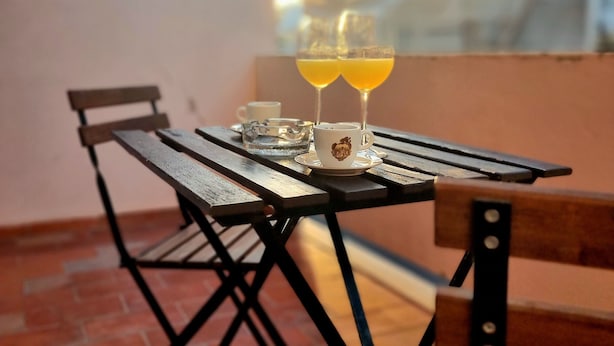 Ein Tisch mit zwei Gläsern Orangensaft, einer Tasse und einem Glas auf einem Balkon mit Blick auf Gebäude.