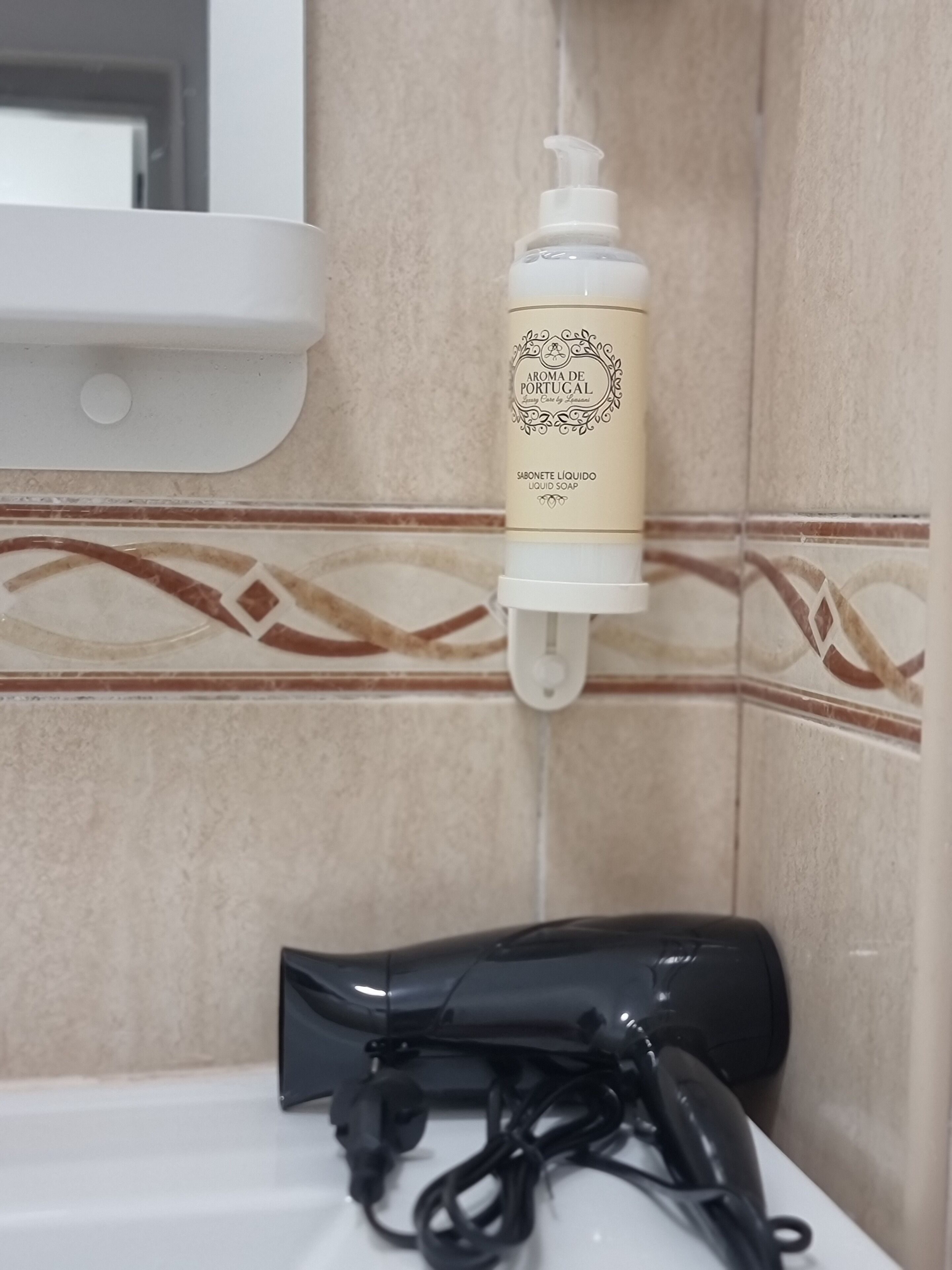 A bathroom with a white sink, a bottle of liquid soap, and a black hairdryer on the counter.