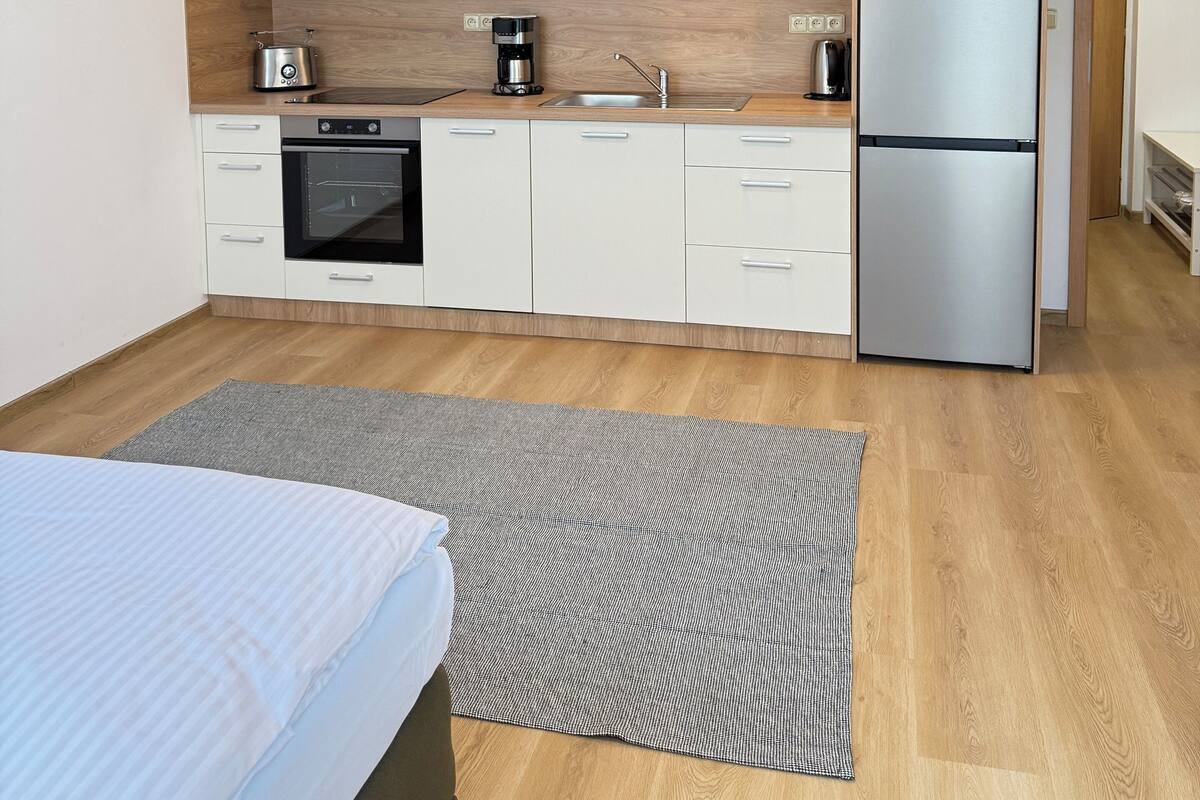 Une cuisine compacte avec des meubles blancs, un four à micro-ondes encastré, un réfrigérateur en acier inoxydable et une machine à café.