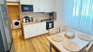 A modern kitchen with white cabinets, a microwave, a coffee maker, and a dishwasher. There is a dining table with woven placemats and chairs. - Parkside Apartments Prague (Prague)