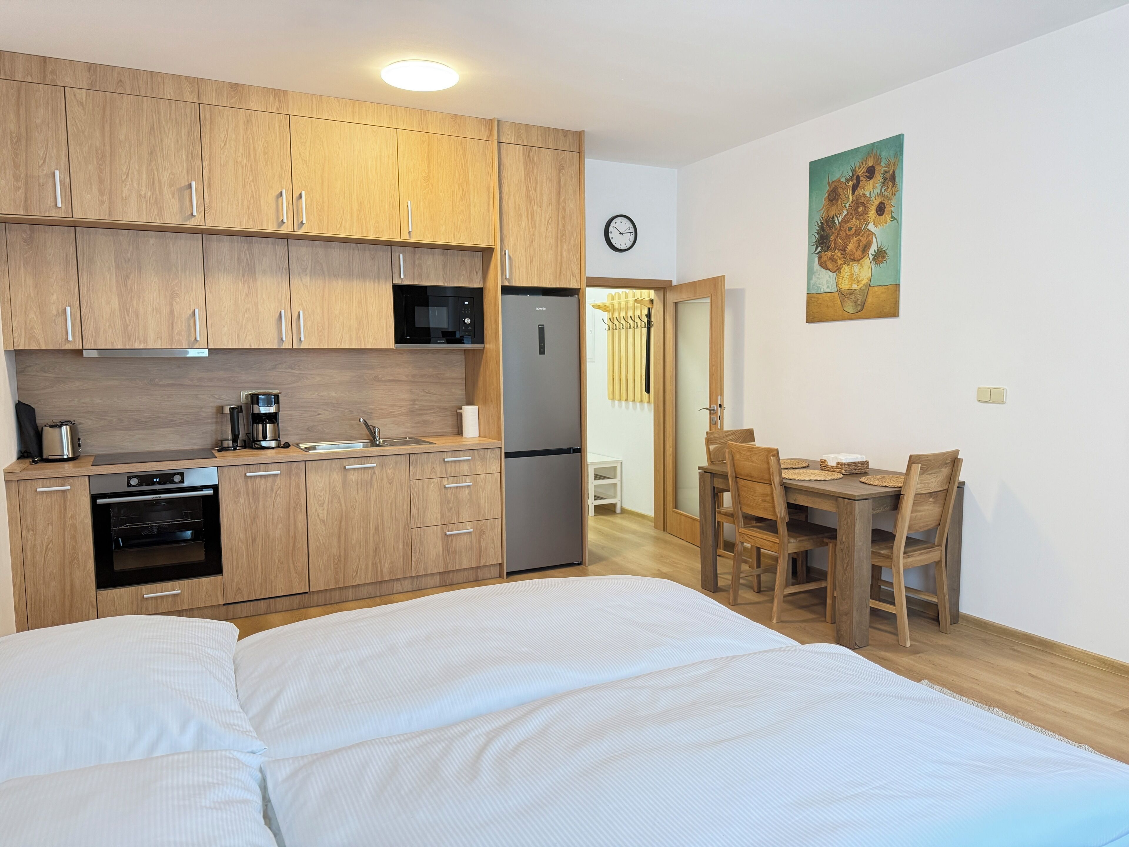 A compact kitchen with wooden cabinets, a microwave, a coffee maker, and a refrigerator. There is a dining area with a wooden table and chairs.