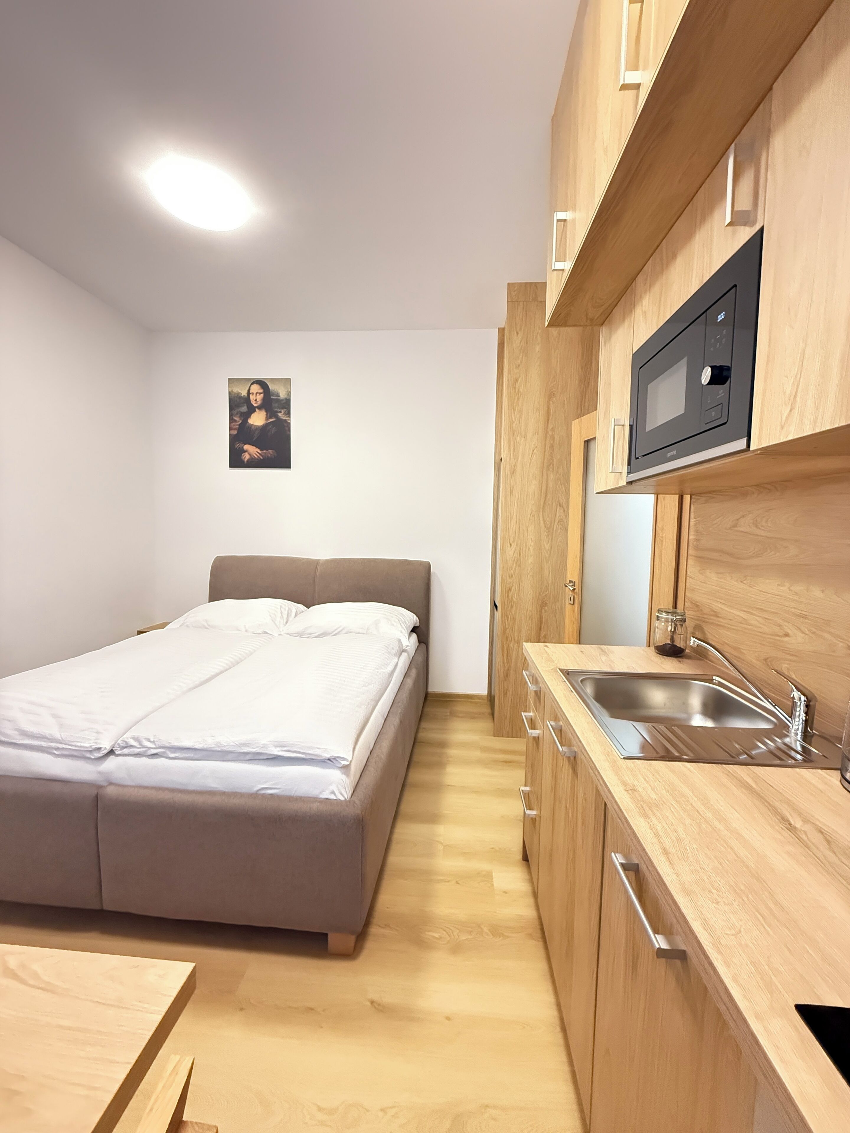Une petite pièce comprenant un lit, un meuble en bois avec un four à micro-ondes, un évier et une petite table.