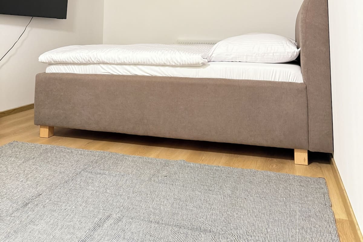 Une chambre à coucher moderne avec un lit, un tapis gris et un téléviseur fixé au mur.
