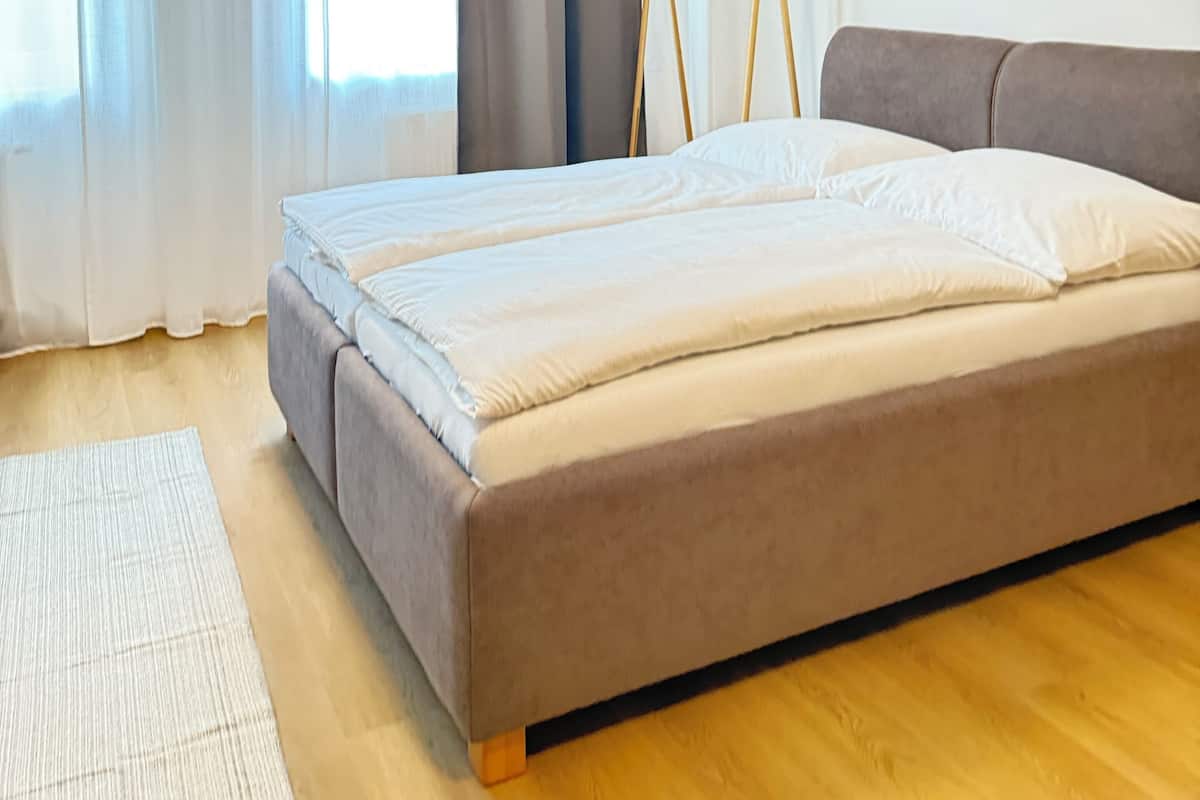 Une chambre à coucher avec un lit, un plancher en bois, une fenêtre avec des rideaux et un luminaire au plafond.