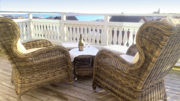 A wicker outdoor seating area with a table and chairs, overlooking a body of water and buildings. - Newly renovated turn-of-the-century house with sea views (Lysekil)