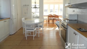 A kitchen with white cabinets, a wooden countertop, a dining table with chairs, and a view of the outside through large windows. - Newly renovated turn-of-the-century house with sea views (Lysekil)