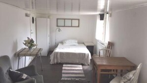 A bedroom with a bed, a small table with a plant, a chair, a desk, and a window.