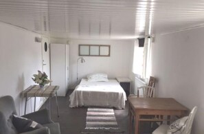 Ein Schlafzimmer mit einem Bett, einem kleinen Tisch mit einer Pflanze, einem Stuhl, einem Schreibtisch und einem Fenster.