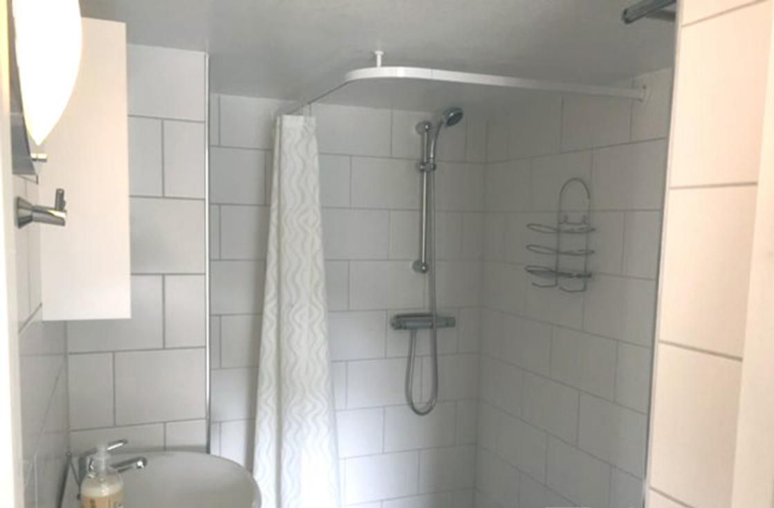 Ein kleines Badezimmer mit einem weißen Waschbecken, einer Dusche und einem Handtuchhalter.