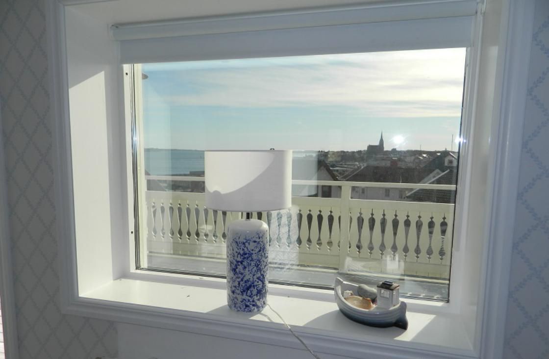 A window with a view of a cityscape, a white radiator below, and a blue and white vase on the windowsill.
