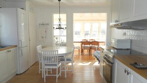 A kitchen with white cabinets, a wooden countertop, a dining table with chairs, and a view of the outside through large windows.