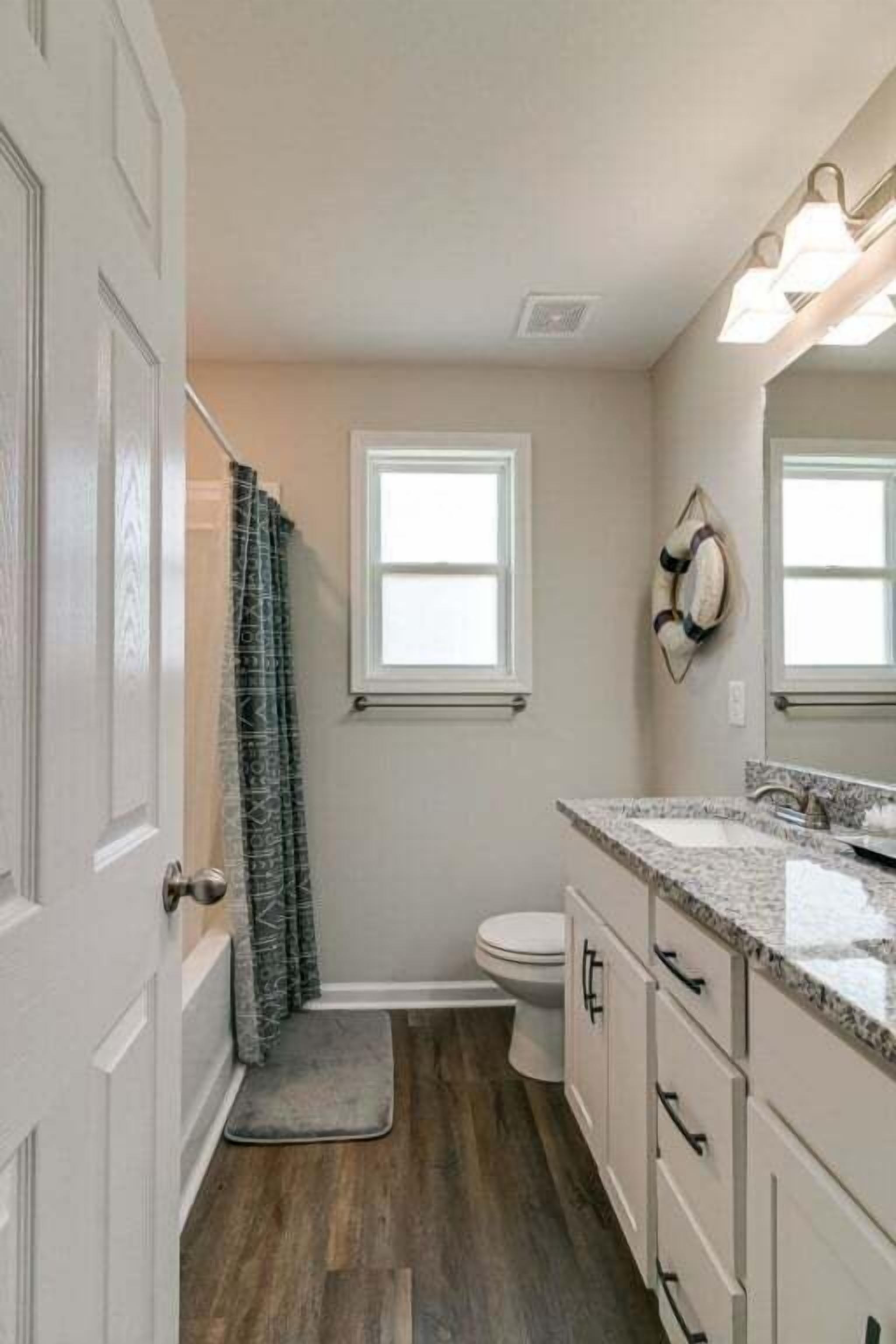 A bathroom with a toilet, a shower curtain, a vanity with a sink, and a mirror.