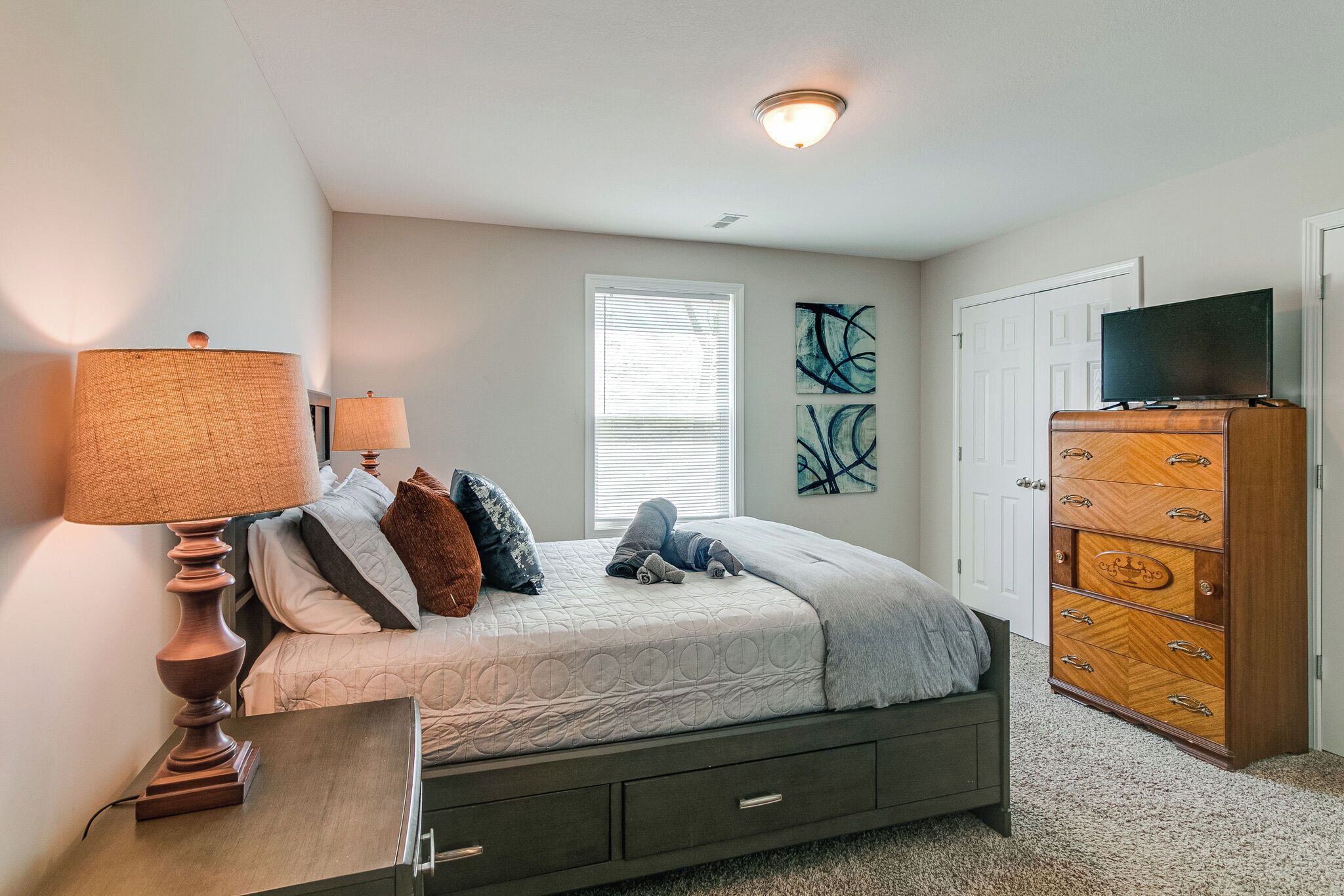 A bedroom with a bed, a dresser, a lamp, and a television.