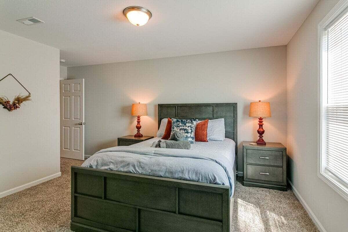 A bedroom with a bed, two bedside tables, a nightstand, a door, and a window with blinds.