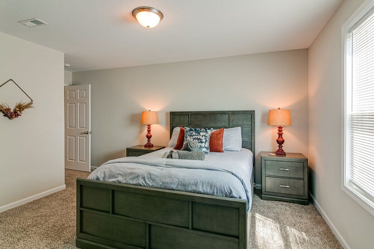 A bedroom with a bed, two bedside tables, a nightstand, a door, and a window with blinds.