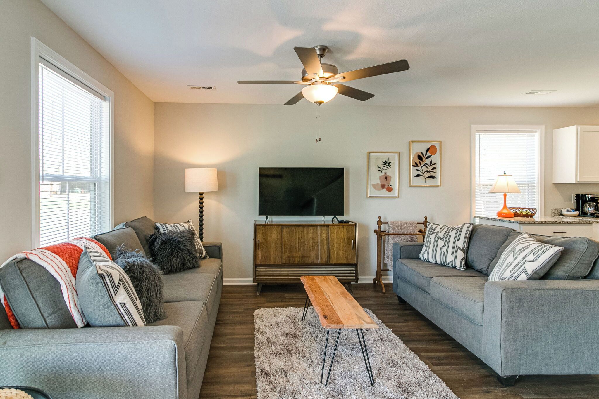 A modern living room with a grey sofa, a wooden coffee table, a TV on a wooden cabinet, and a ceiling fan.