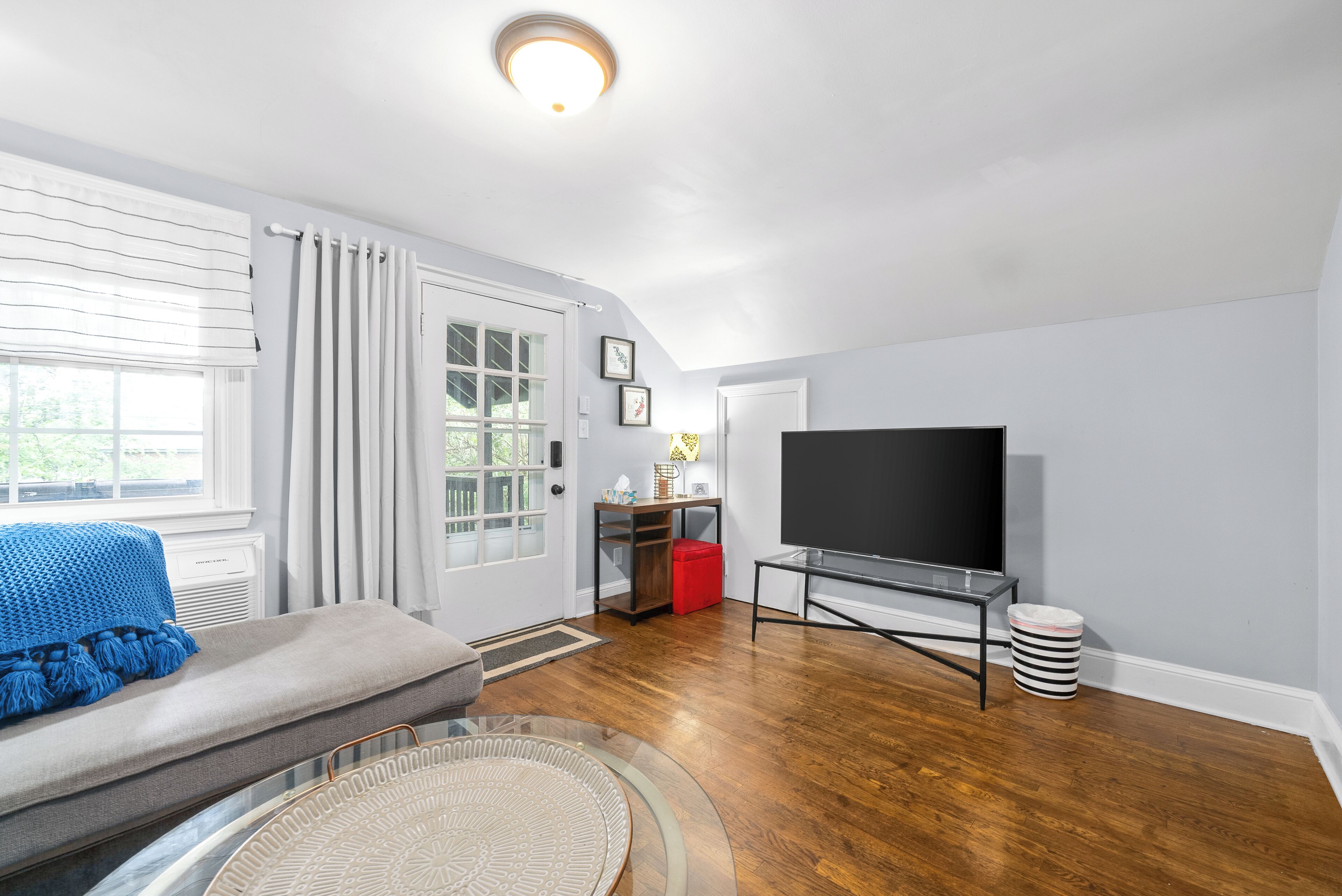 A living room with a sofa, a television on a stand, a door, and a window.