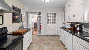 A kitchen with white cabinets, a black stove, and a tiled floor.