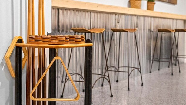 A row of bar stools with a woven top table, metal legs, and a wooden counter with plants.