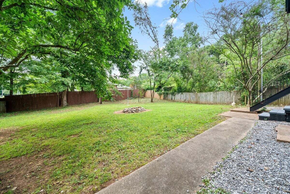 A backyard with a grassy lawn, a concrete path, and a wooden fence.