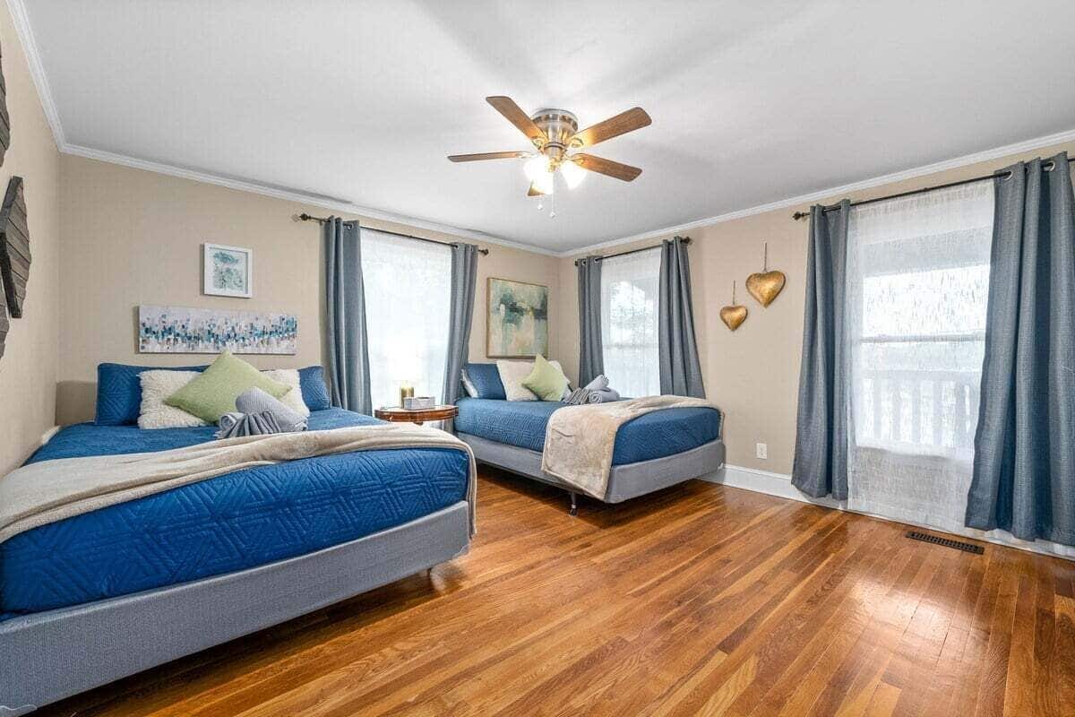 Quarto com duas camas, ventilador de teto e uma janela grande com cortinas.