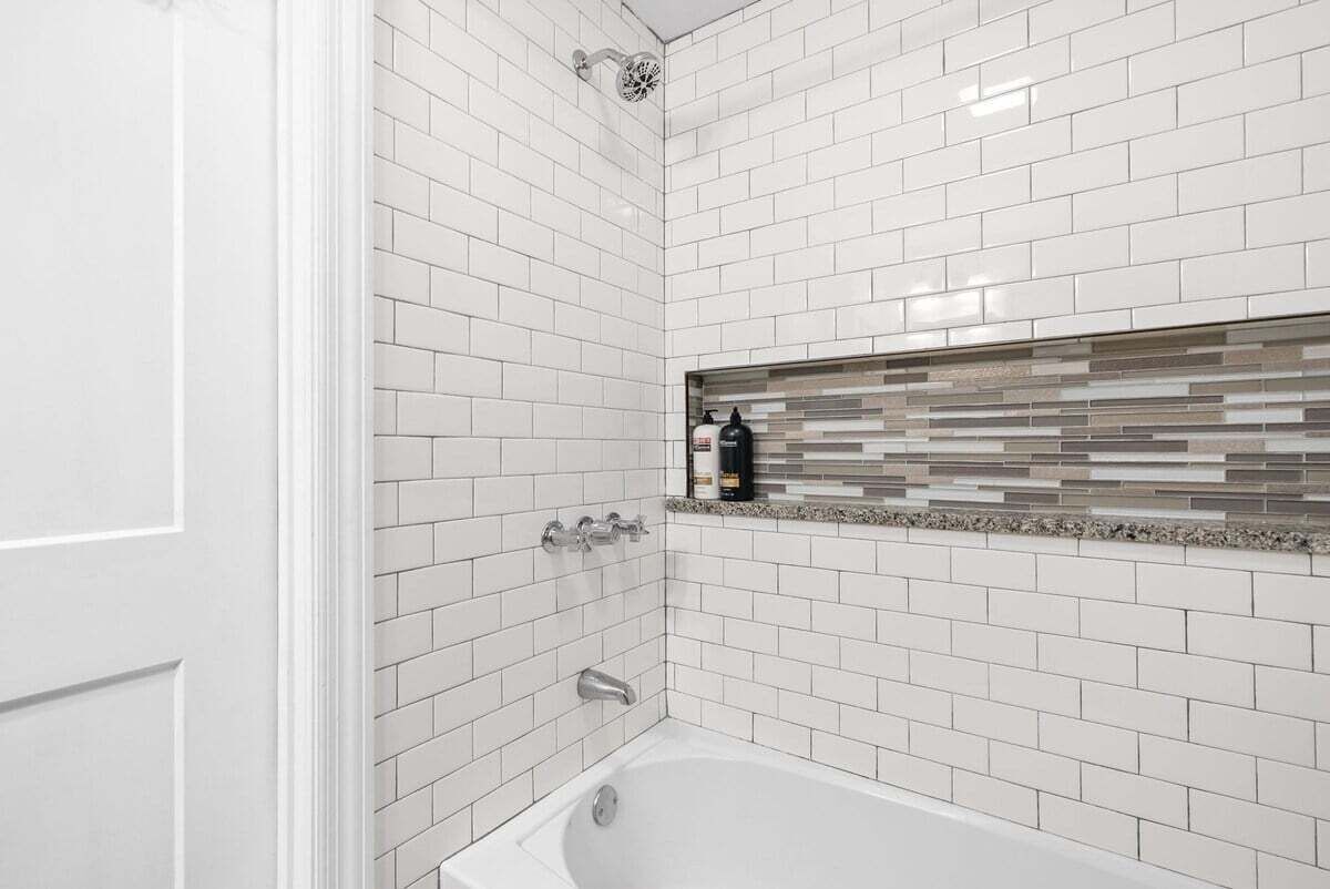 A bathroom with white subway tiles, a glass shower enclosure, and a built-in shelf with toiletries.