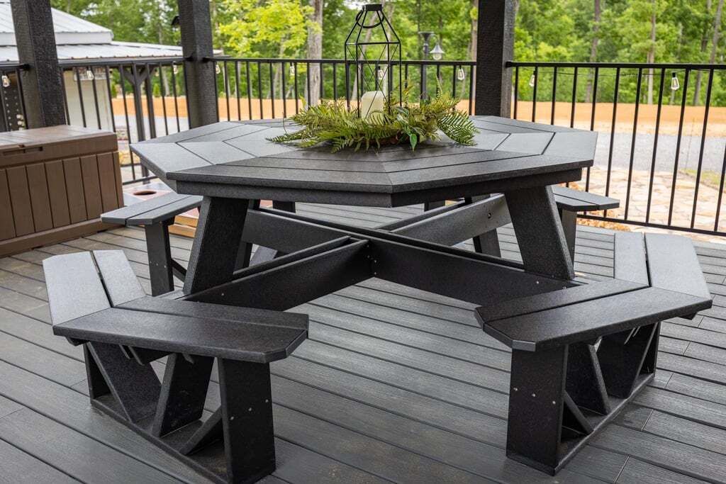 Una terraza de madera oscura con una mesa hexagonal y bancos, rodeada por una barandilla de metal negro.