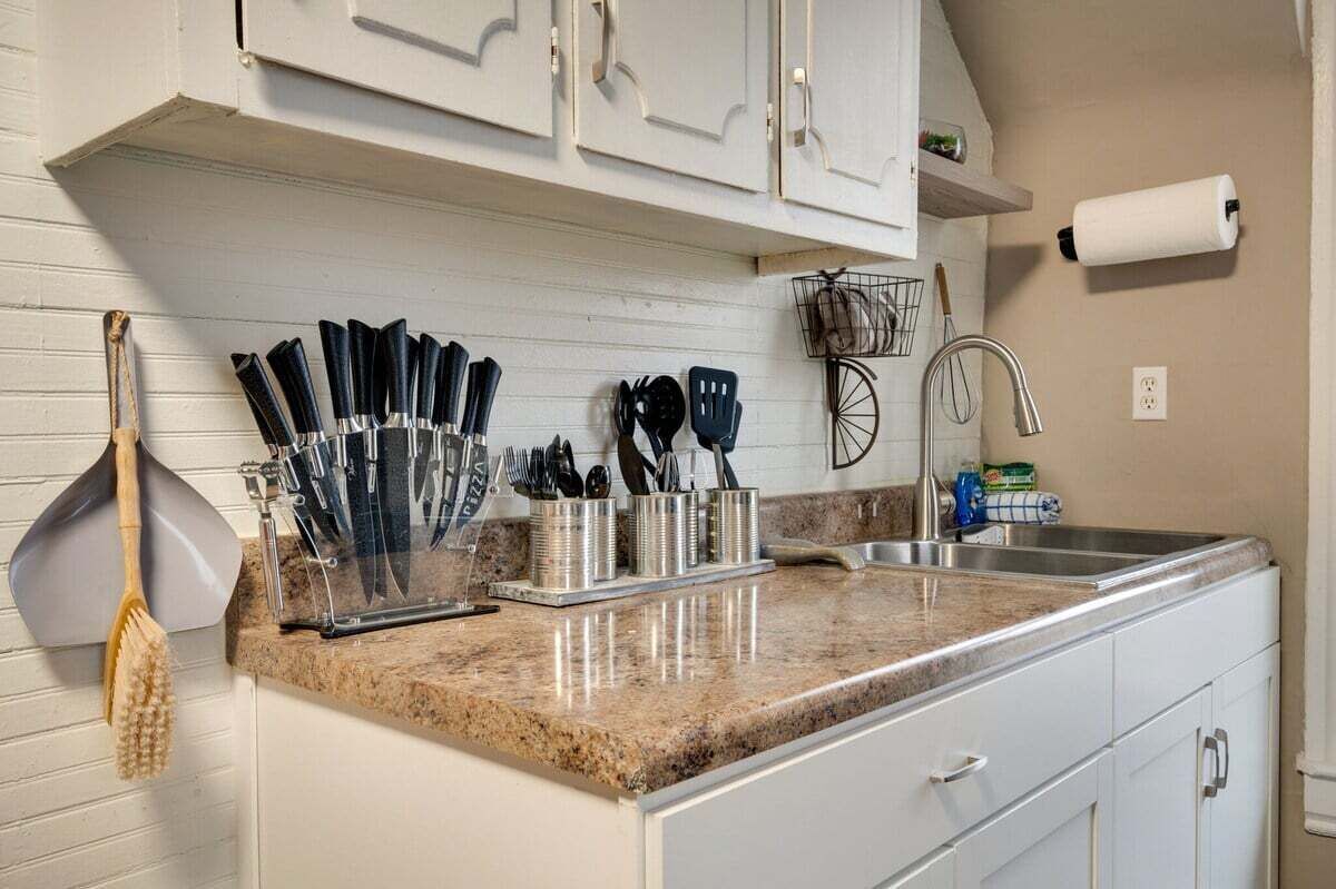 Una cocina con armarios blancos, encimera de granito y diferentes utensilios.