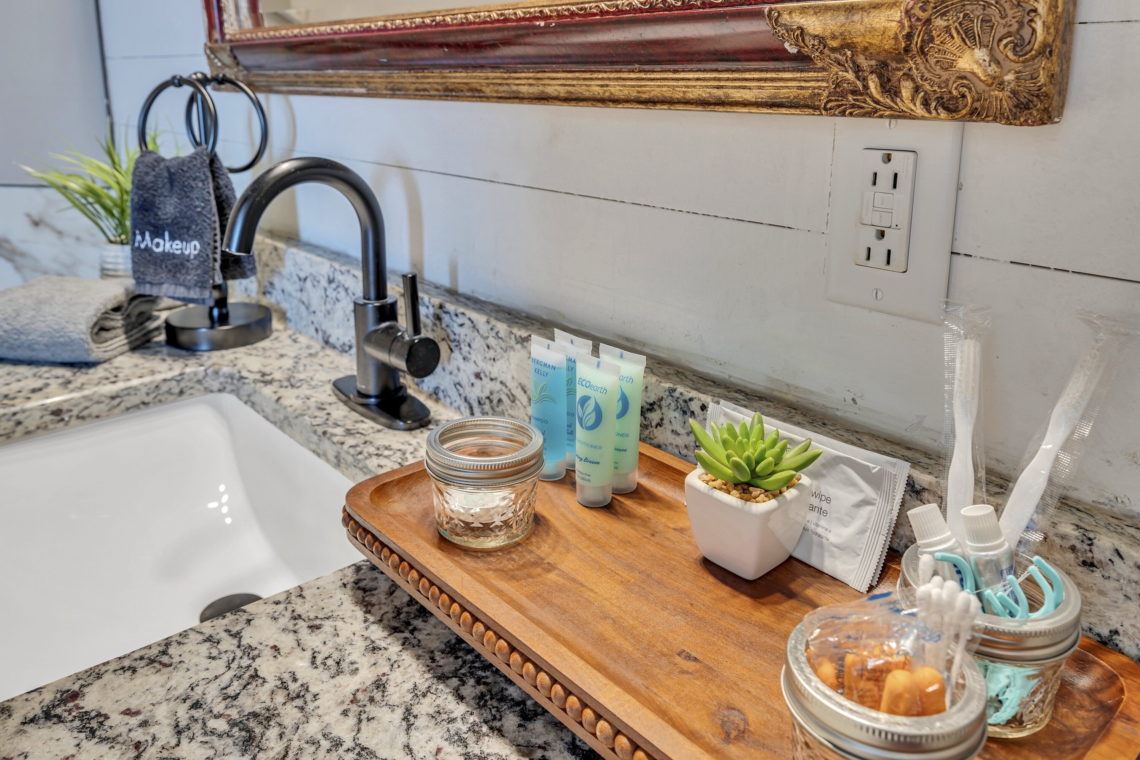 A bathroom with a granite countertop, a sink, a mirror with an ornate frame, and a tray with toiletries.