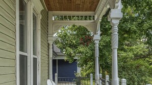 A wooden porch with two white chairs, a wooden railing, and a view of a blue house in the background. - Marion Street (Clarksville)