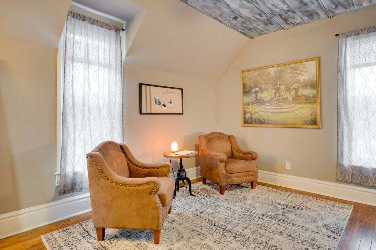 Una stanza con due poltrone in pelle, un tavolino con una lampada, una fotografia incorniciata e un grande dipinto raffigurante un paesaggio sulla parete.