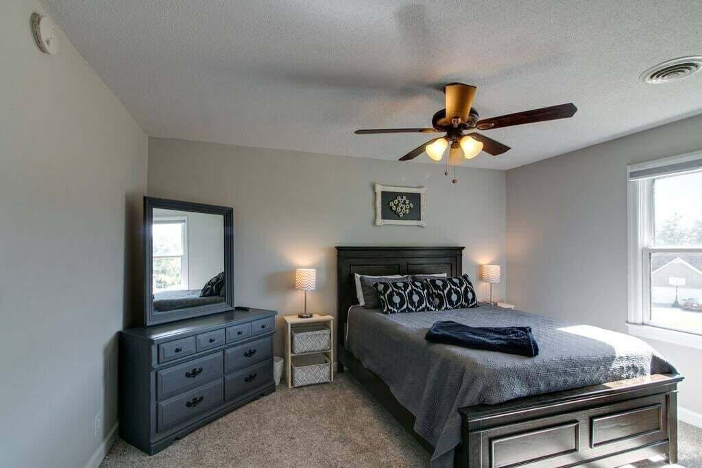 A bedroom with a bed, a dresser, a mirror, a ceiling fan, and a window.
