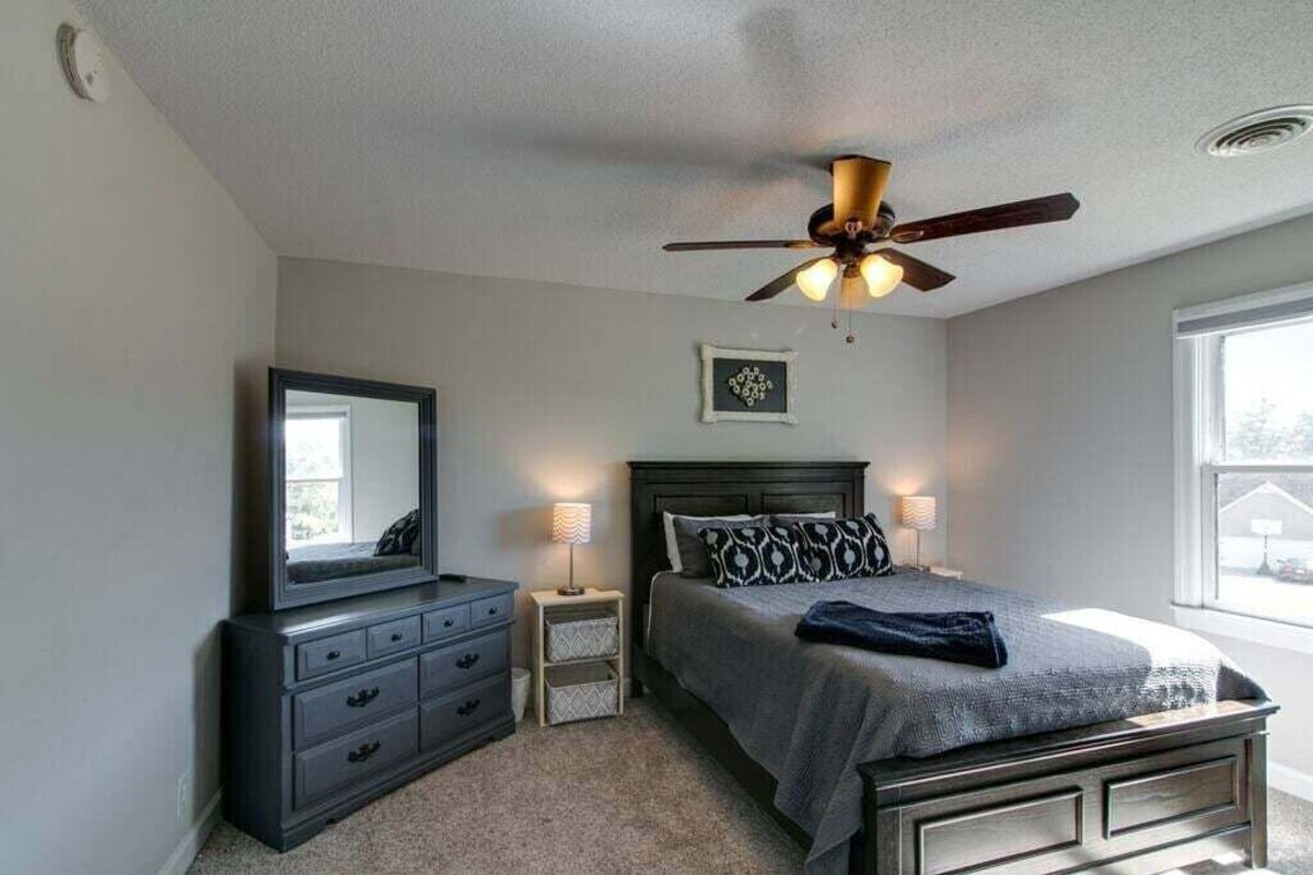A bedroom with a bed, a dresser, a mirror, a ceiling fan, and a window.