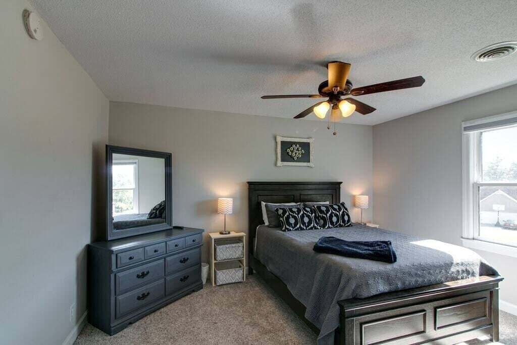 A bedroom with a bed, a dresser, a mirror, a ceiling fan, and a window.