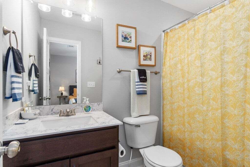 Ein Badezimmer mit Toilette, einem Waschbecken mit Marmorplatte und einer Duschkabine mit gelbem Blumenmuster.