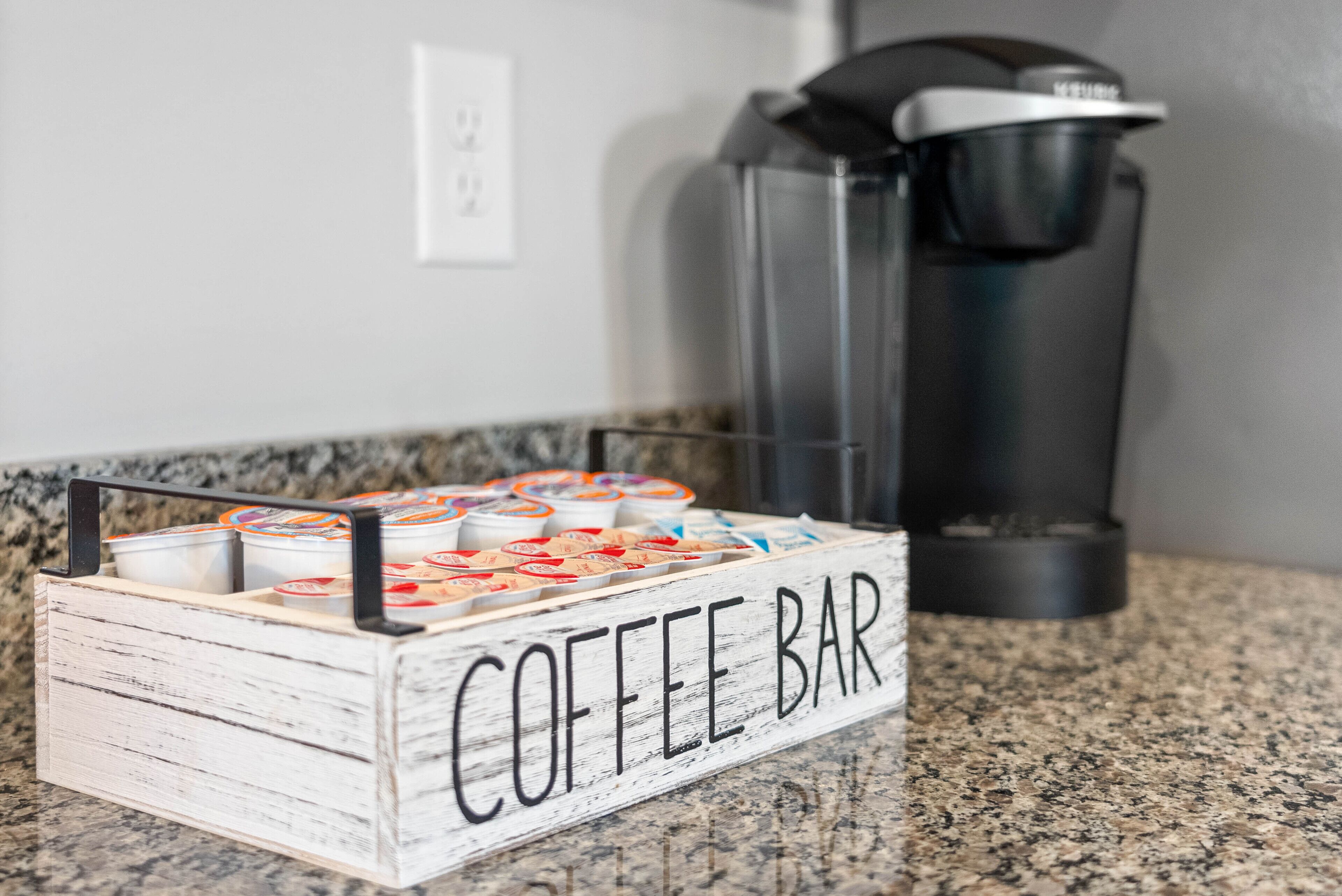 Mostrador de cafetería con un letrero, recipientes de café y una máquina de café.