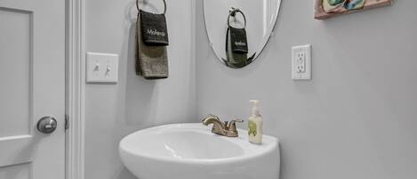A bathroom with a white pedestal sink, a mirror, and a wall-mounted light fixture.