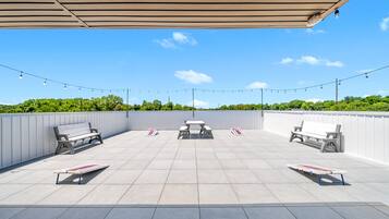 Un patio techado al aire libre con dos bancos y una mesa de picnic, rodeado por un muro bajo y luces colgantes.
