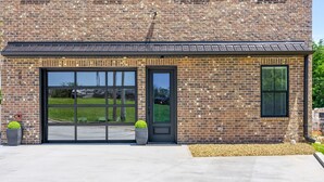 A brick building with a large garage door and a small door, surrounded by a concrete driveway and two potted plants. - The Spot (Clarksville)