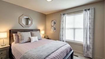 A bedroom with a bed, bedside tables, a mirror, and a window with curtains.