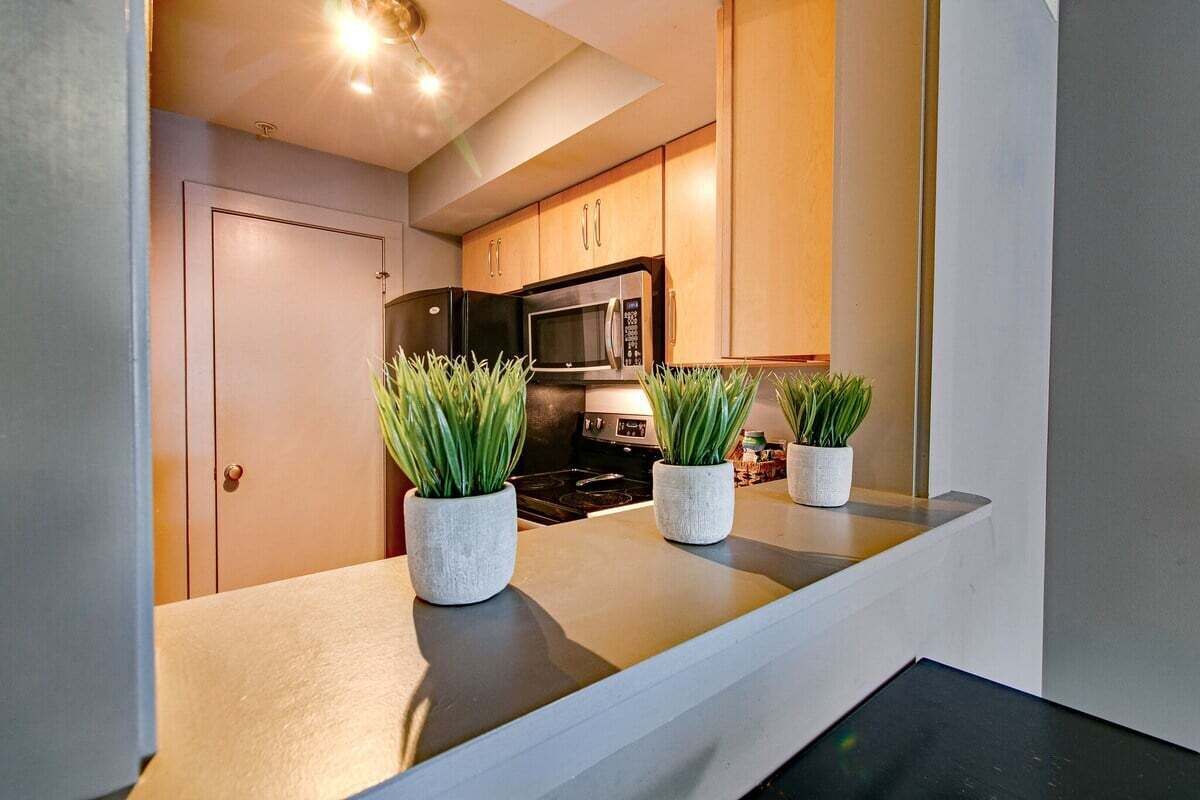 A modern kitchen with wooden cabinets, a microwave, and a stove. There are three potted plants on the countertop.