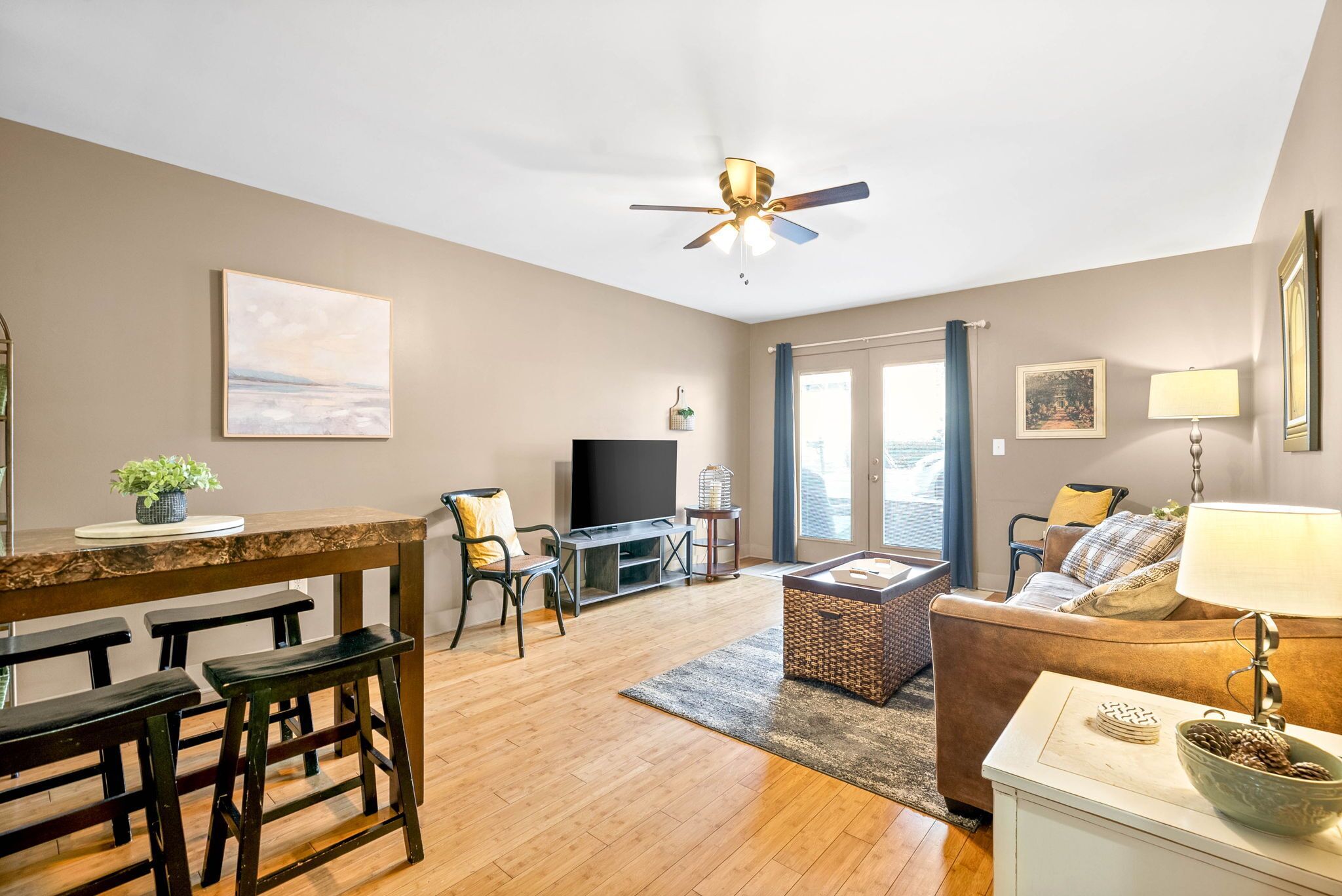 A living room with a wooden floor, a ceiling fan, a television, a sofa, a coffee table, and a dining area with benches and a table.