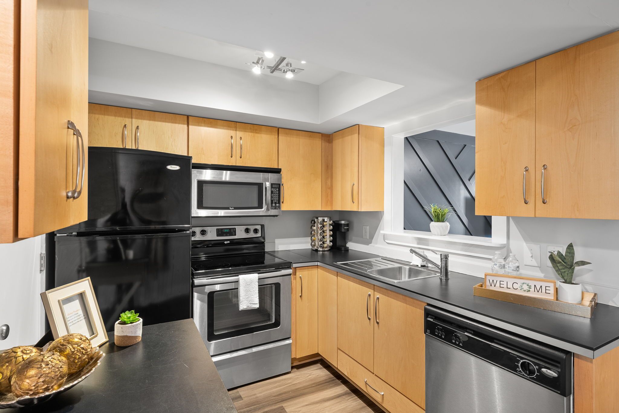 A modern kitchen with wooden cabinets, stainless steel appliances, and a black countertop.
