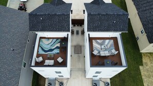 A two-story house with a covered patio area on the upper floor, featuring outdoor seating and a large rug. - Adam's Downtown Retreat w/ Rooftop Access (Clarksville)