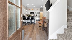 A modern kitchen with white cabinets, a stainless steel refrigerator, and a dining area with a wooden table and chairs. - Adam's Downtown Retreat w/ Rooftop Access (Clarksville)