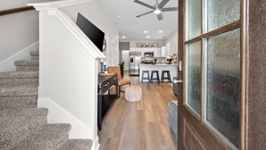A modern kitchen with a central island, a dining area with a wooden table and chairs, and a staircase leading to an upper level. - Urban Rooftop of Downtown (Clarksville)