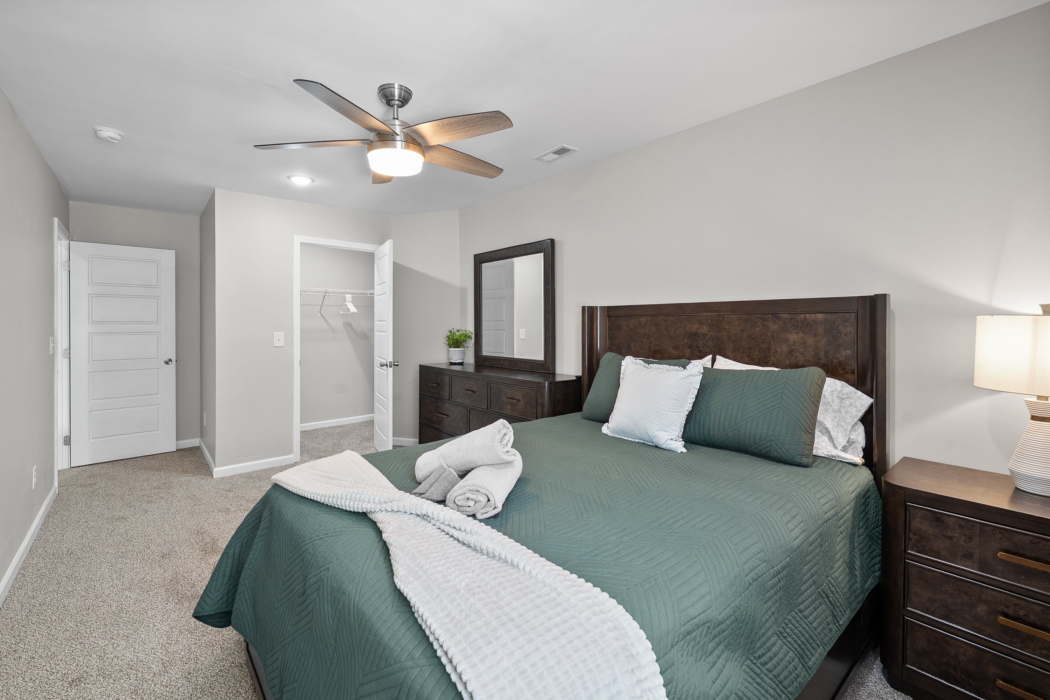 Une chambre à coucher comprenant un lit, une table de chevet, une commode, un ventilateur de plafond et une porte.